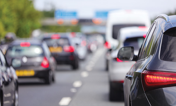 traffic jam on the highway with multiple vehicles including cars and vans displaying brake lights in the foreground reflecting the five lanes of congestion