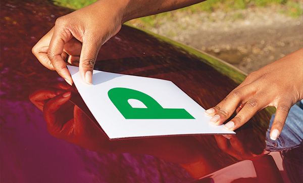 hands applying P plate to car roof in preparation for driving lessons to achieve 5 essential skills