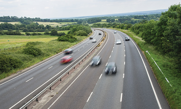 aerial view of a highway with moving cars surrounded by green fields and trees highlighting nine lanes of traffic in a rural landscape