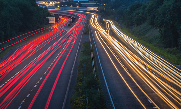 long exposure shot of a busy highway at night showing red and white light trails from vehicles illustrating the flow of traffic with three lanes visible