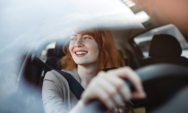 smiling woman driving a car enjoying a fun ride in urban environment with four wheels