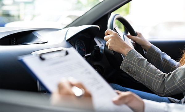 person holding steering wheel while another hands over a clipboard with driving instructions related to driving test tips and seven key points