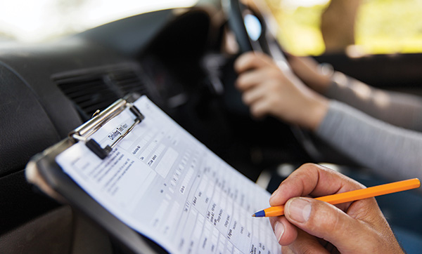 person holding a clipboard with a driving assessment checklist while observing a person driving a car safety driving evaluation