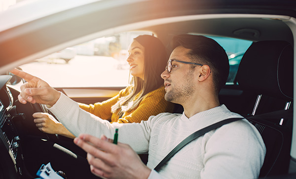 a man and woman inside a car the man is pointing while the woman drives they appear engaged in conversation promoting safe driving tips for the next 5 lessons